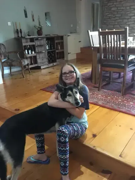 Girl hugging a black and white dog on a wooden floor