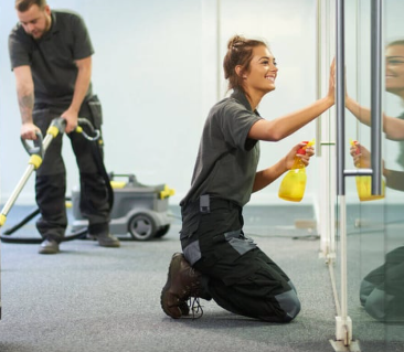 A man and a woman are cleaning a room with a vacuum cleaner and a spray bottle.
