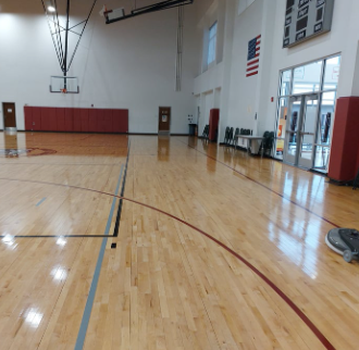 An empty gym with a basketball hoop and an american flag on the wall