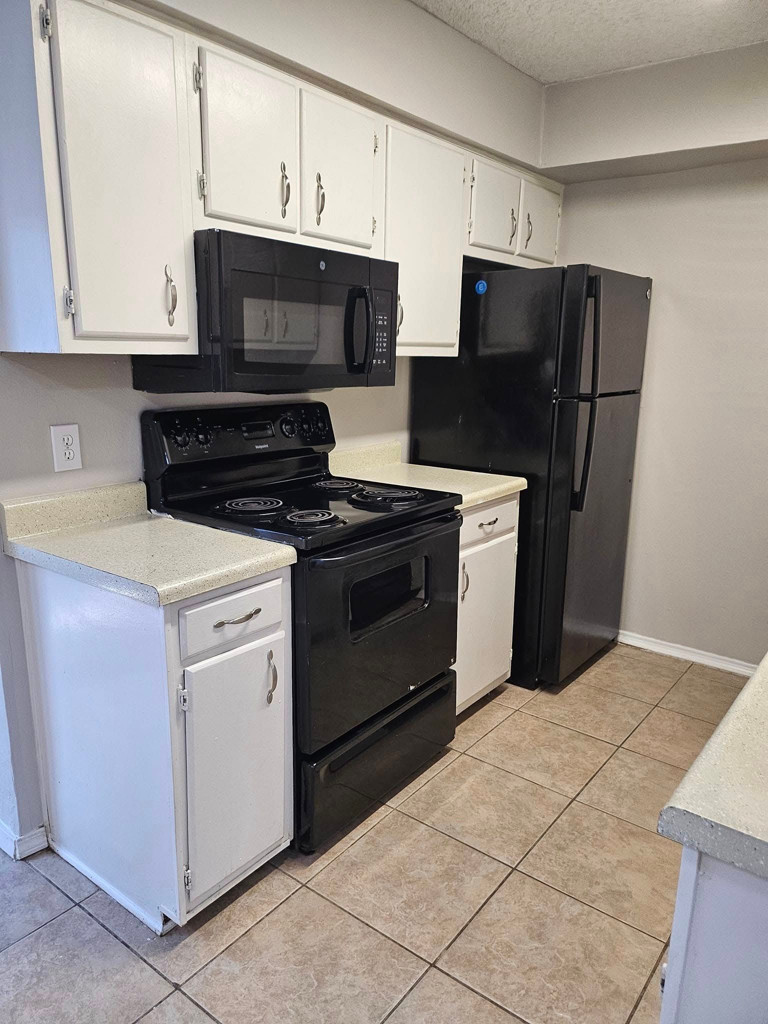 A kitchen with a stove , refrigerator , microwave and white cabinets.