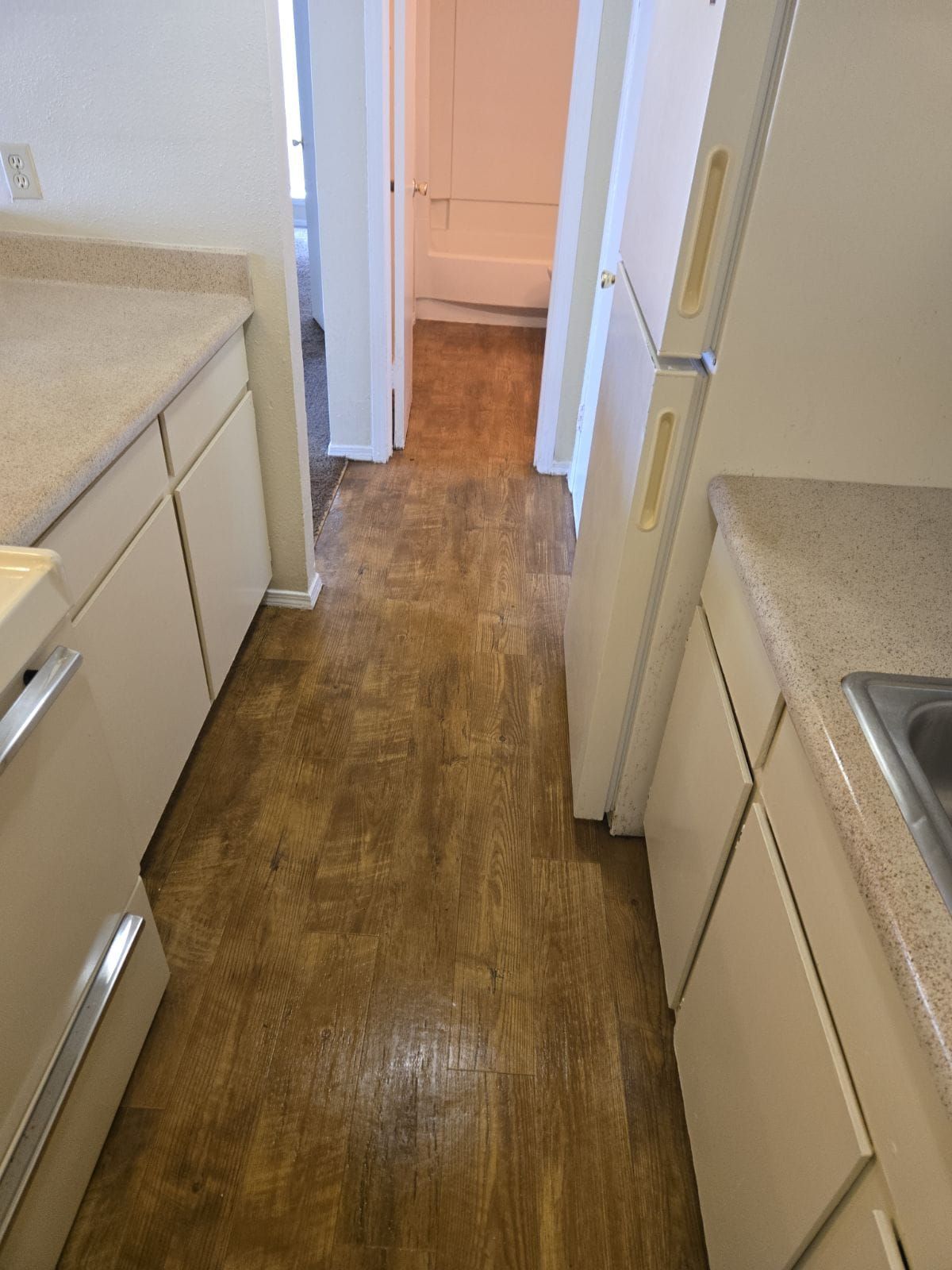 A kitchen with wooden floors and white cabinets and a refrigerator.