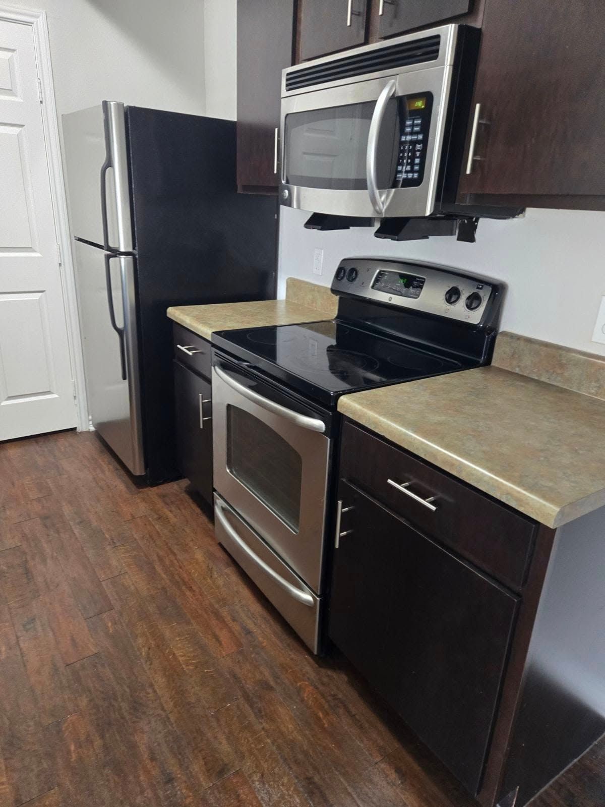 A kitchen with a stove , microwave , refrigerator and cabinets.