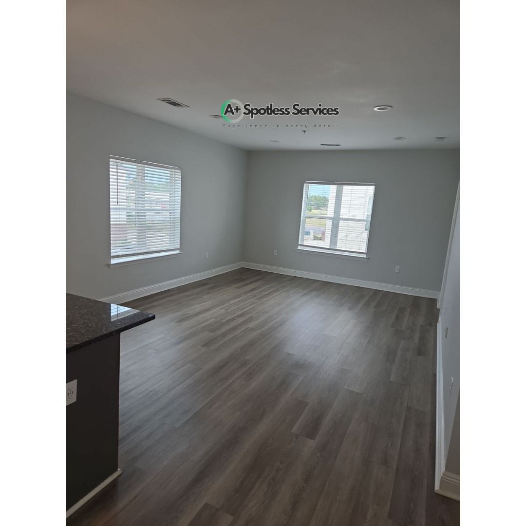 An empty living room with hardwood floors and two windows.