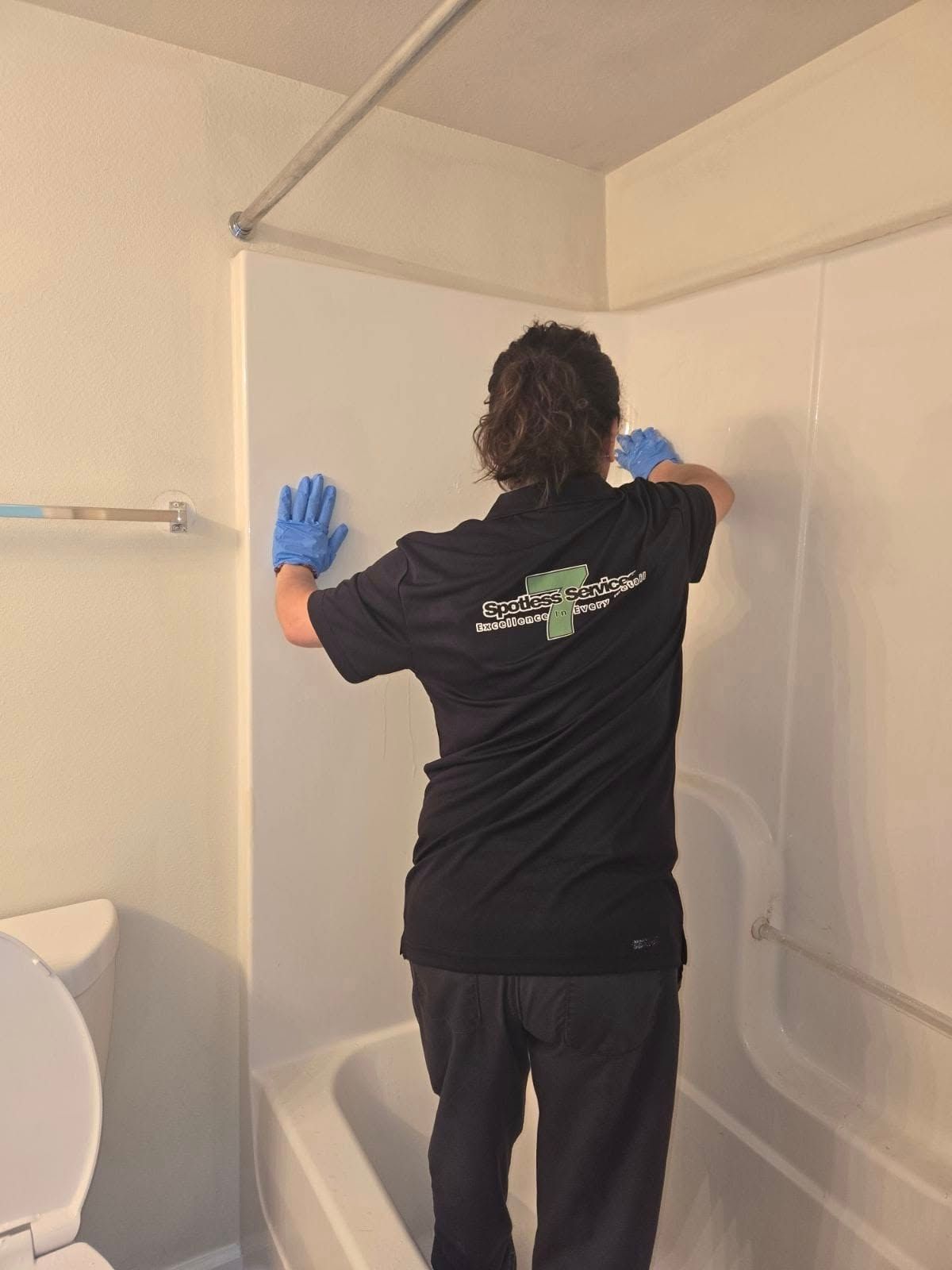 A man in a black shirt is cleaning a shower wall in a bathroom.