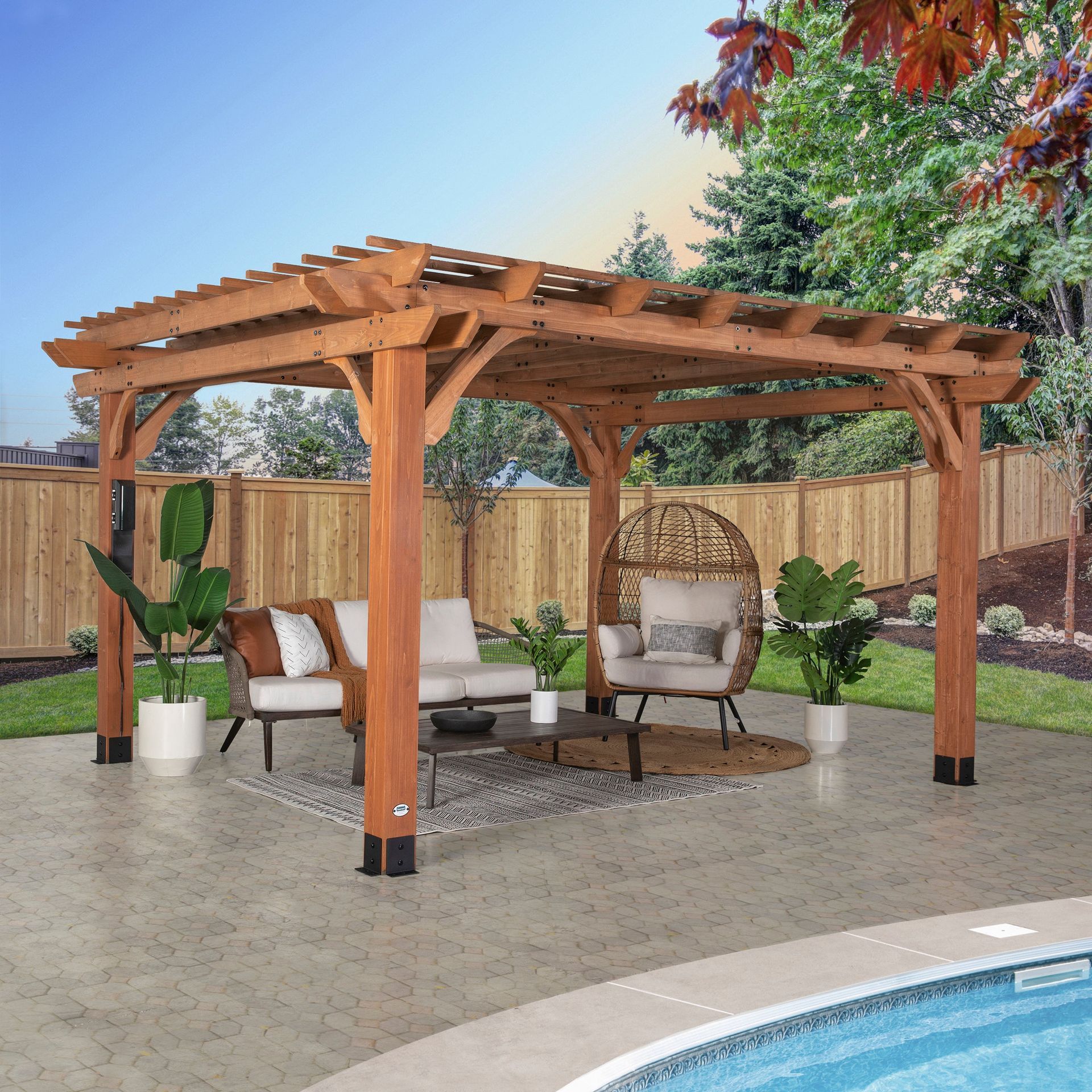Wooden pergola over patio furniture near a pool, set against a wooden fence and trees.