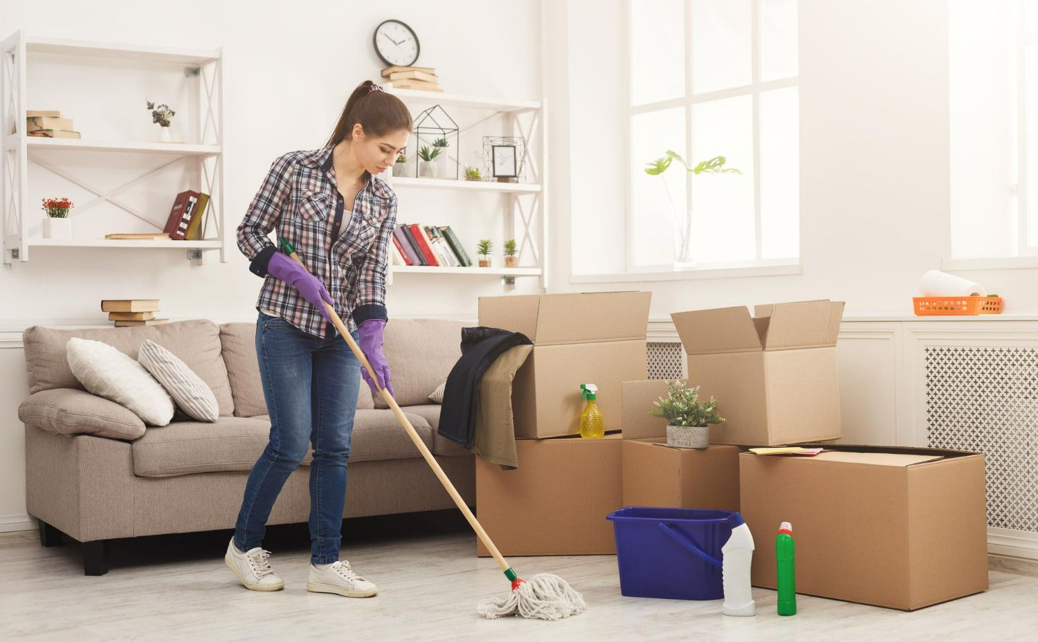 A woman is cleaning the floor of a living room with a mop.