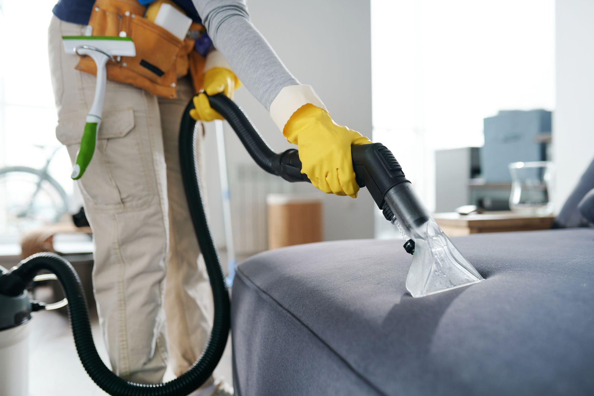 A person is cleaning a couch with a vacuum cleaner.