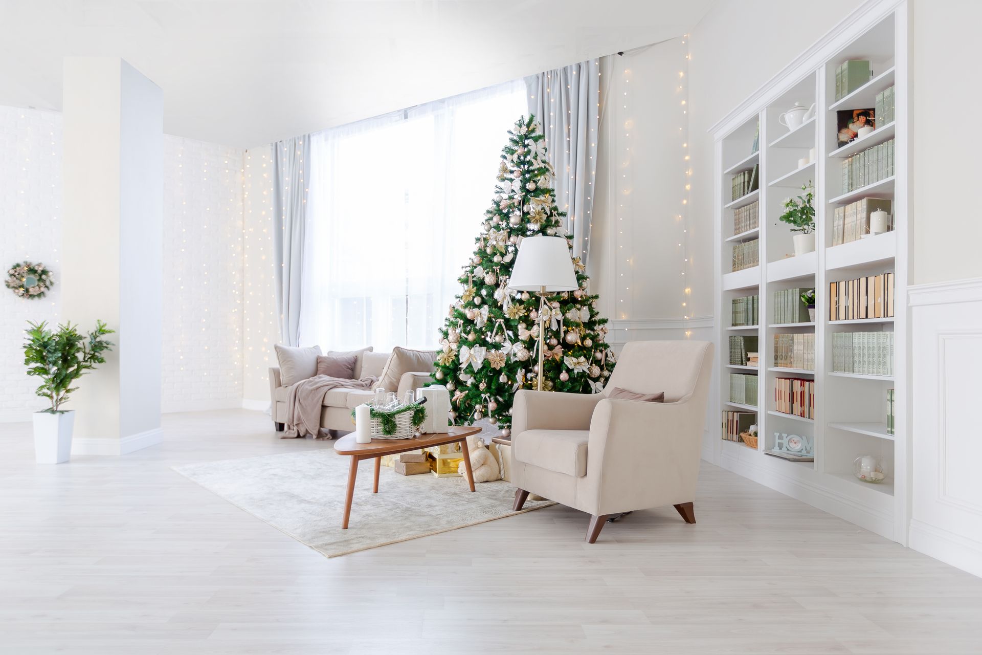 Cozy, bright living room decorated for Christmas; tree, sofa, armchair, bookshelves.