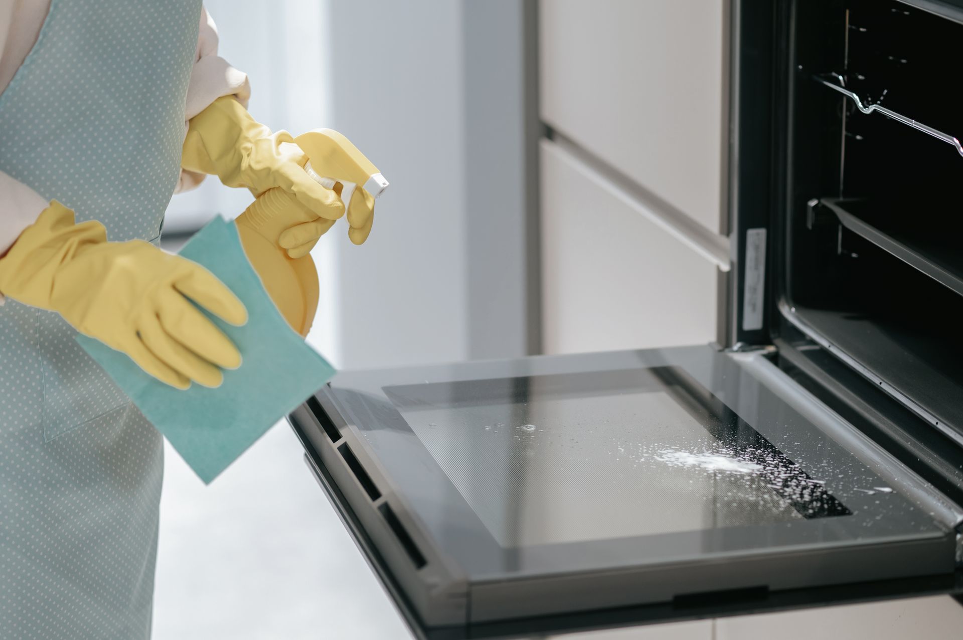 A person is cleaning an oven with a spray bottle and a cloth.