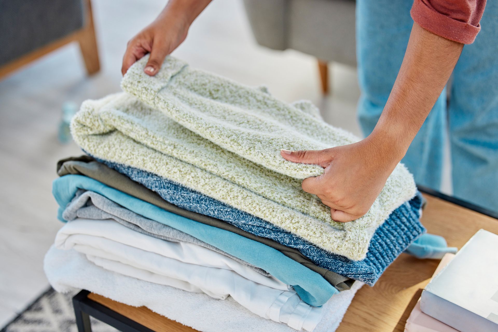 Person folding clothes, a stack of various colored garments on a table.