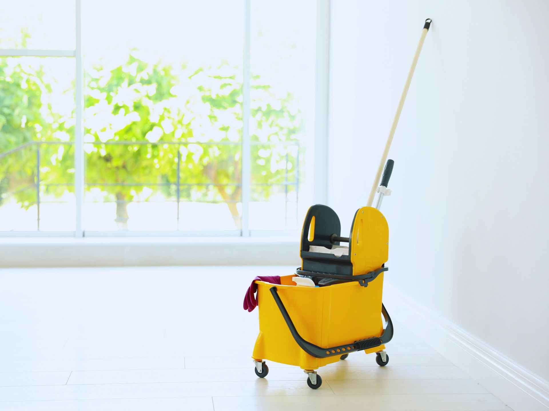 A yellow mop and bucket are sitting on a white floor in an empty room.