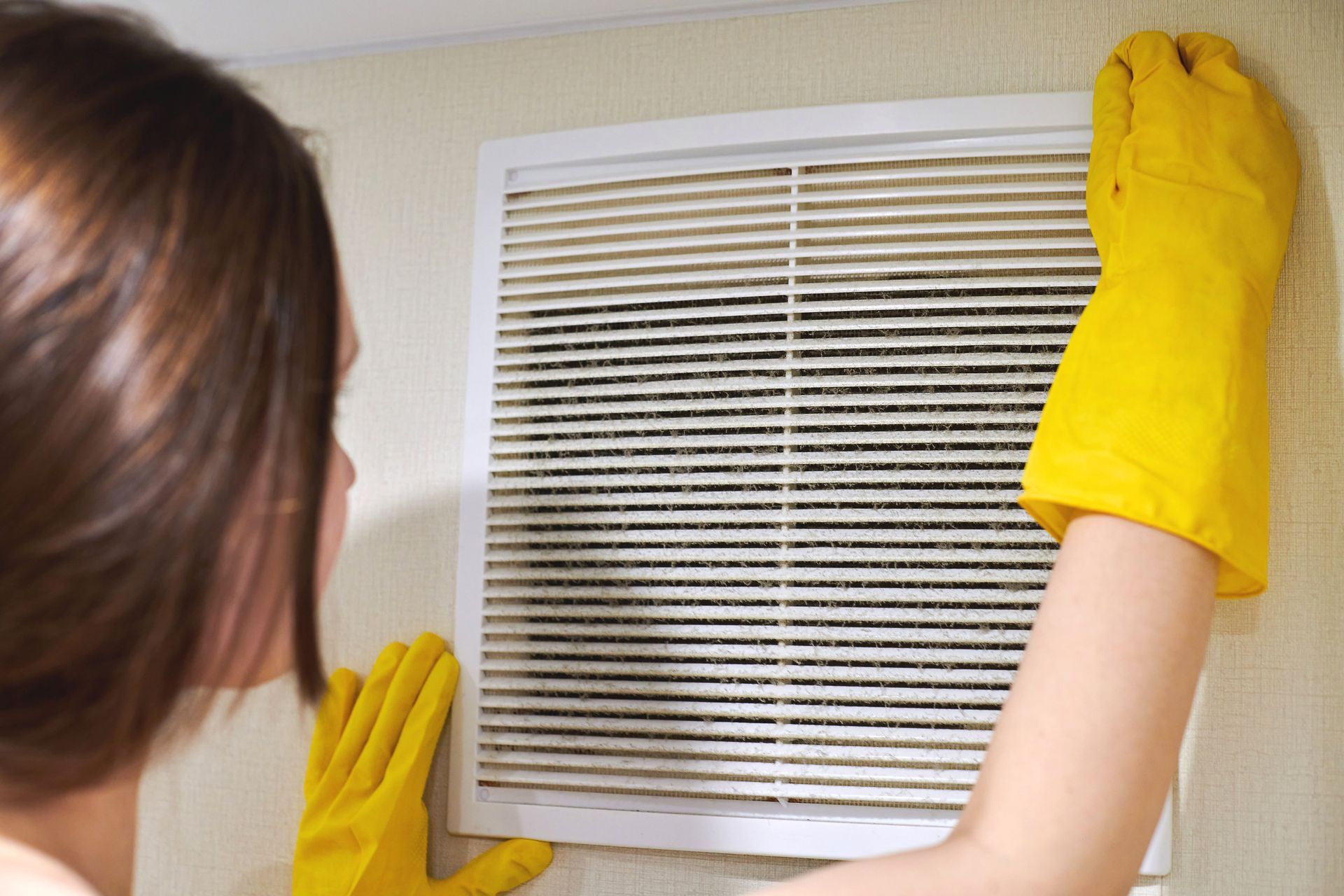 woman with yellow gloves cleaning an air vent