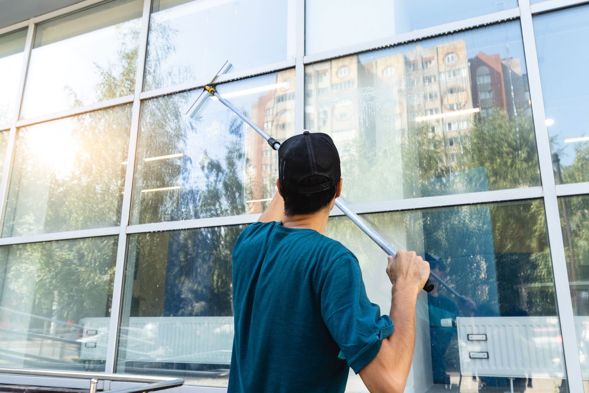 Worker cleaning large glass windows with a squeegee outdoors