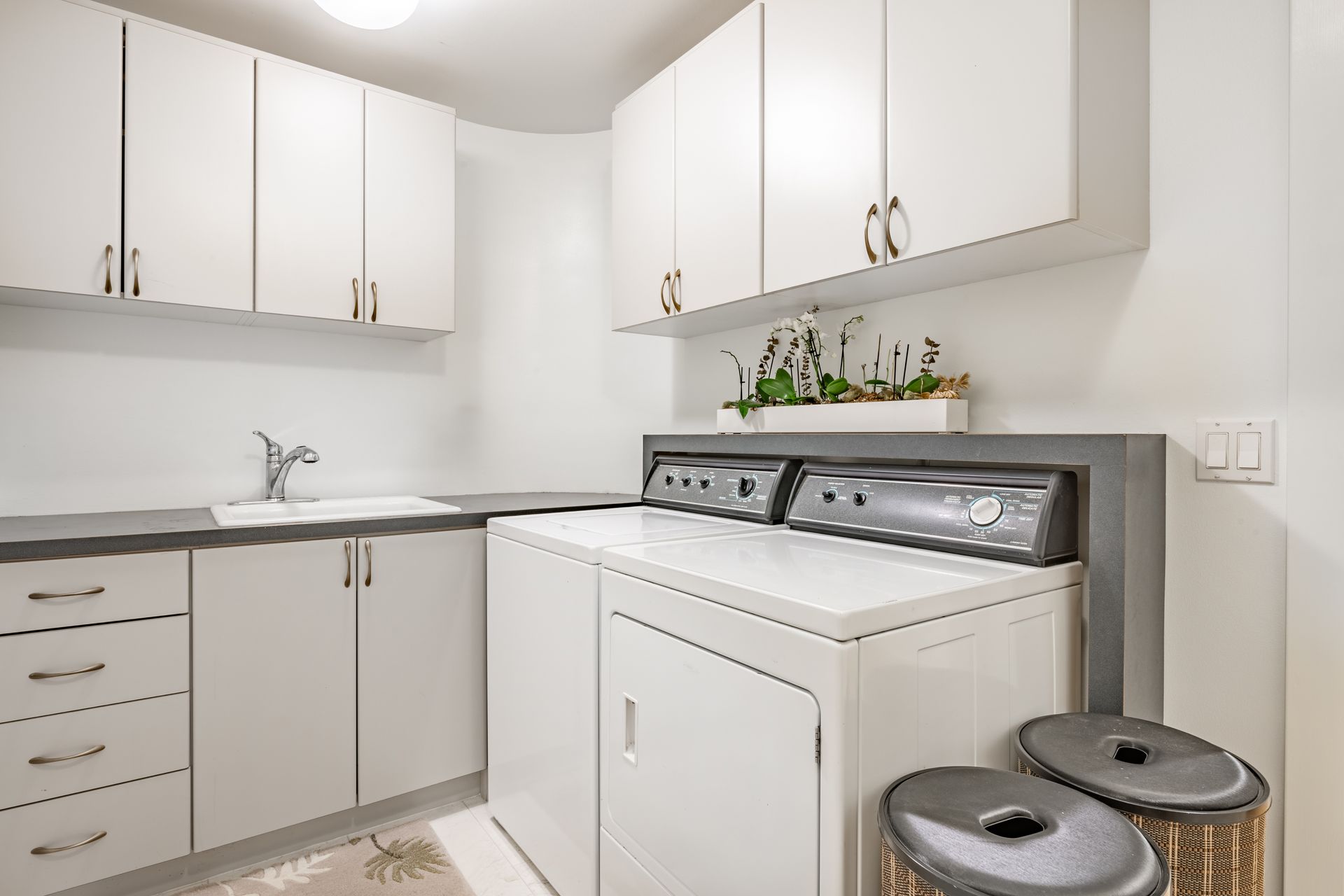 Bright laundry room with white cabinets, gray countertops, and a washer and dryer.