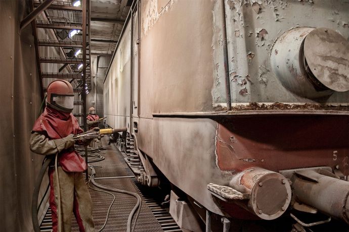 A man is sandblasting a train car in a factory