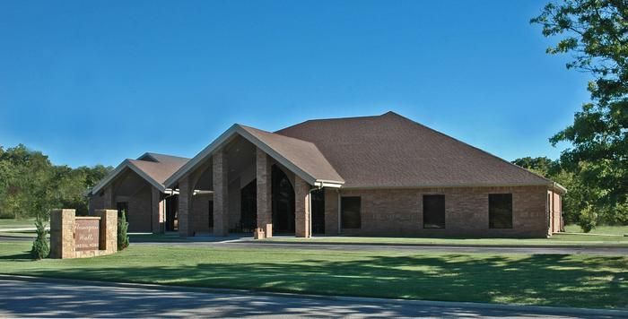 A low-rise brick building with a brown roof and a sign on a green lawn against a blue sky.