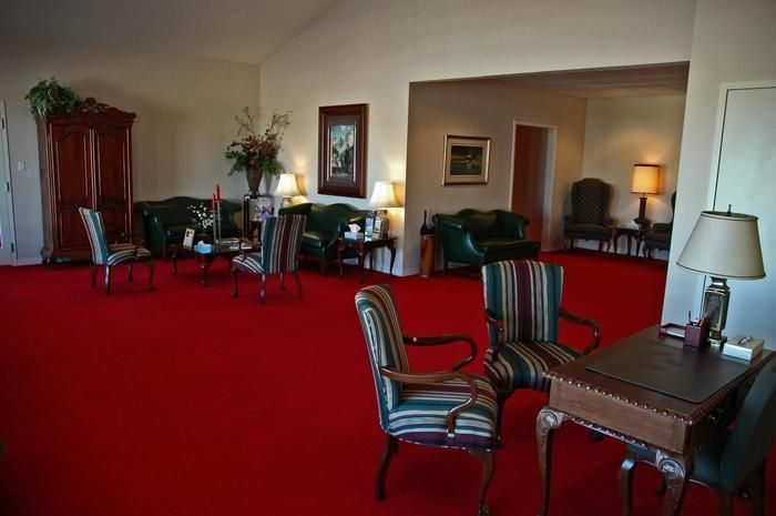 Red-carpeted waiting room with green leather sofas, chairs, wooden cabinet, and lamps.