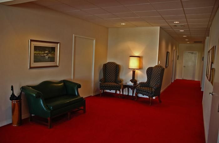 Hallway with red carpet, leather seating, and two ornate chairs.