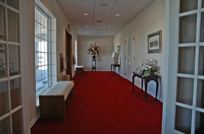 Hallway with red carpet, white walls, and floral arrangements.