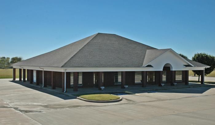 Brick building with white columns and a covered porch on a sunny day.