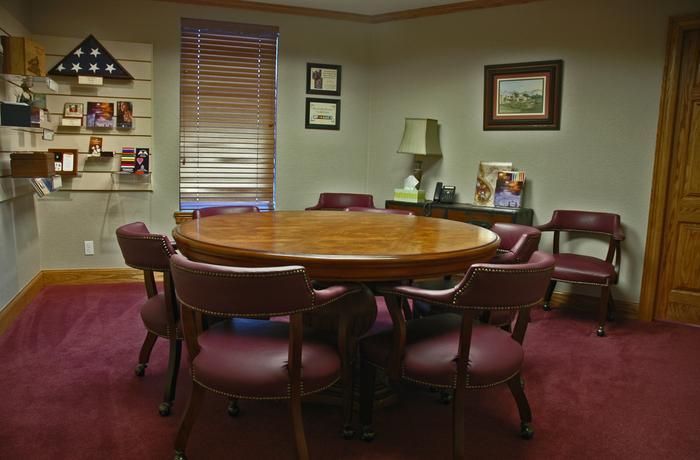 A burgundy carpeted room with a round wooden table surrounded by red chairs, and a display of photos.