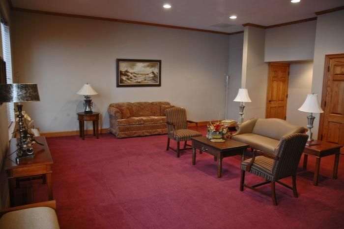 A furnished waiting room with red carpet, two sofas, two chairs, several lamps, and a painting.