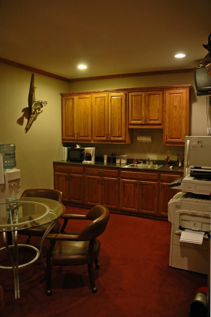 Office break room with wooden cabinets, a table, and a water cooler on a red carpet.