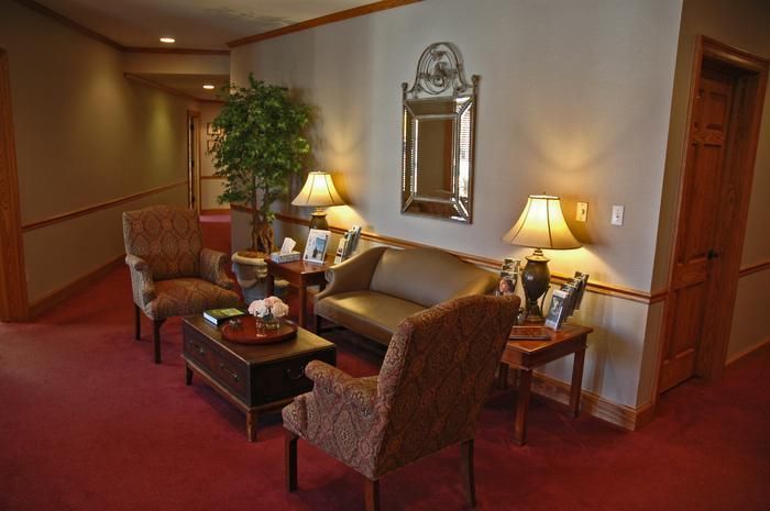Waiting room with chairs, sofa, lamps, and a mirror on a red carpet.