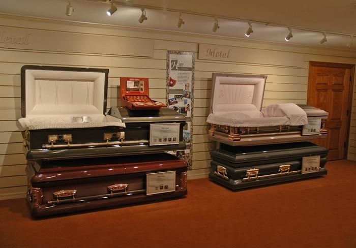 Coffins displayed in a showroom with open lids, various colors, and price tags.