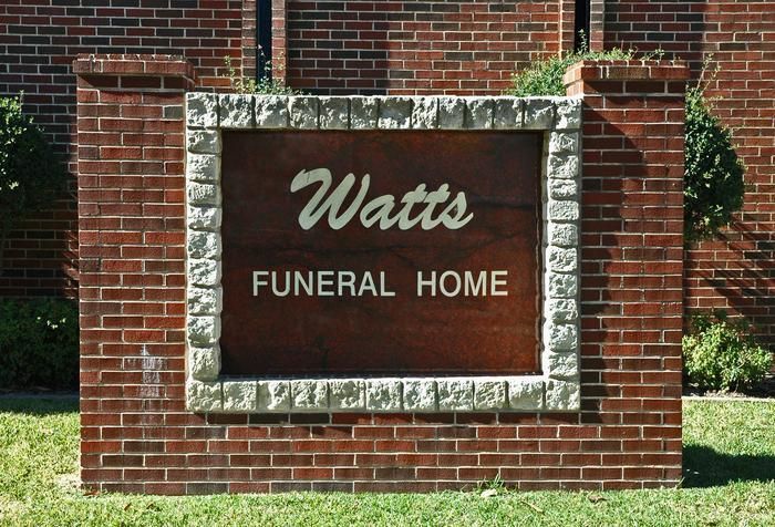 Sign for Watts Funeral Home, red brick with a brown sign and white lettering.