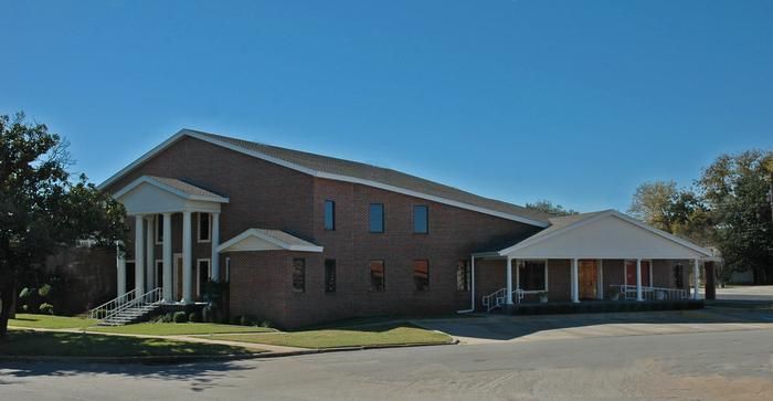 Brick building with white columns and a covered porch on a sunny day.