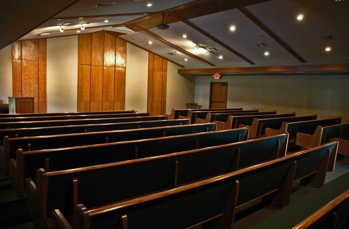 Empty church auditorium with rows of wooden pews, wooden panels, and a sloped ceiling.