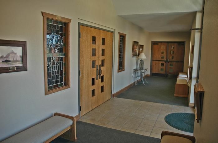 Hallway with light-colored walls, wood doors, stained glass windows, and a bench.