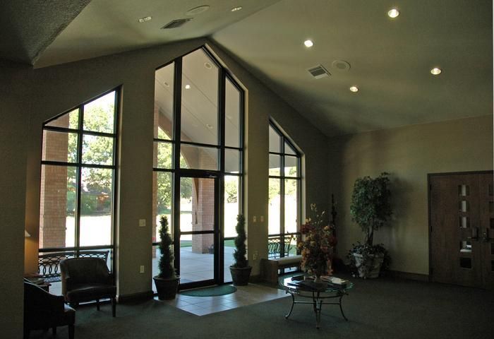 A bright lobby with large triangular windows, a potted plant, and a seating area with a table.