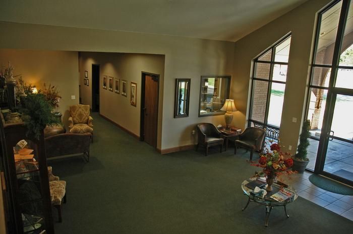 Interior waiting room with green carpet, seating, artwork, and large windows.