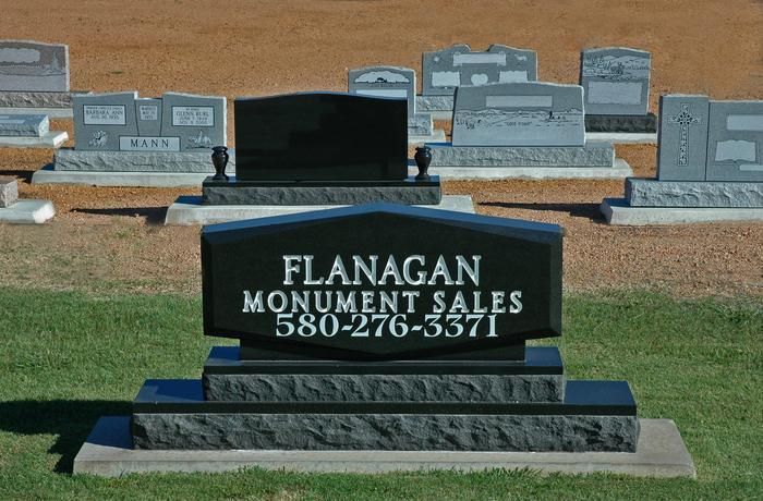 Black Flanagan Monument Sales headstone with phone number displayed in a cemetery.
