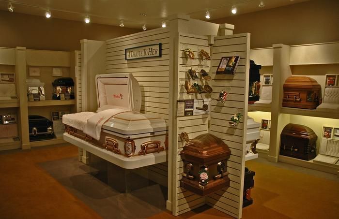 Funeral home interior with coffins on display. White and brown wood coffins, various shapes.
