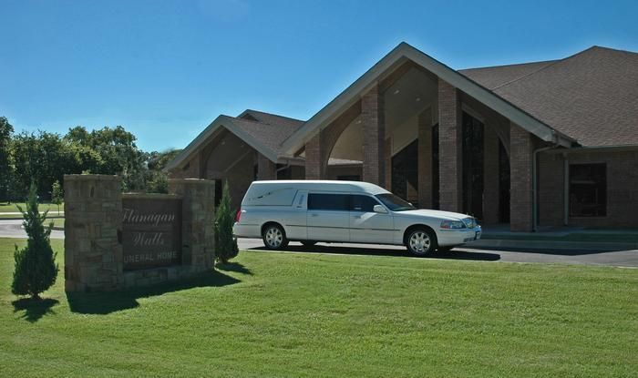 White hearse parked in front of a brick building with a sign and manicured lawn on a sunny day.