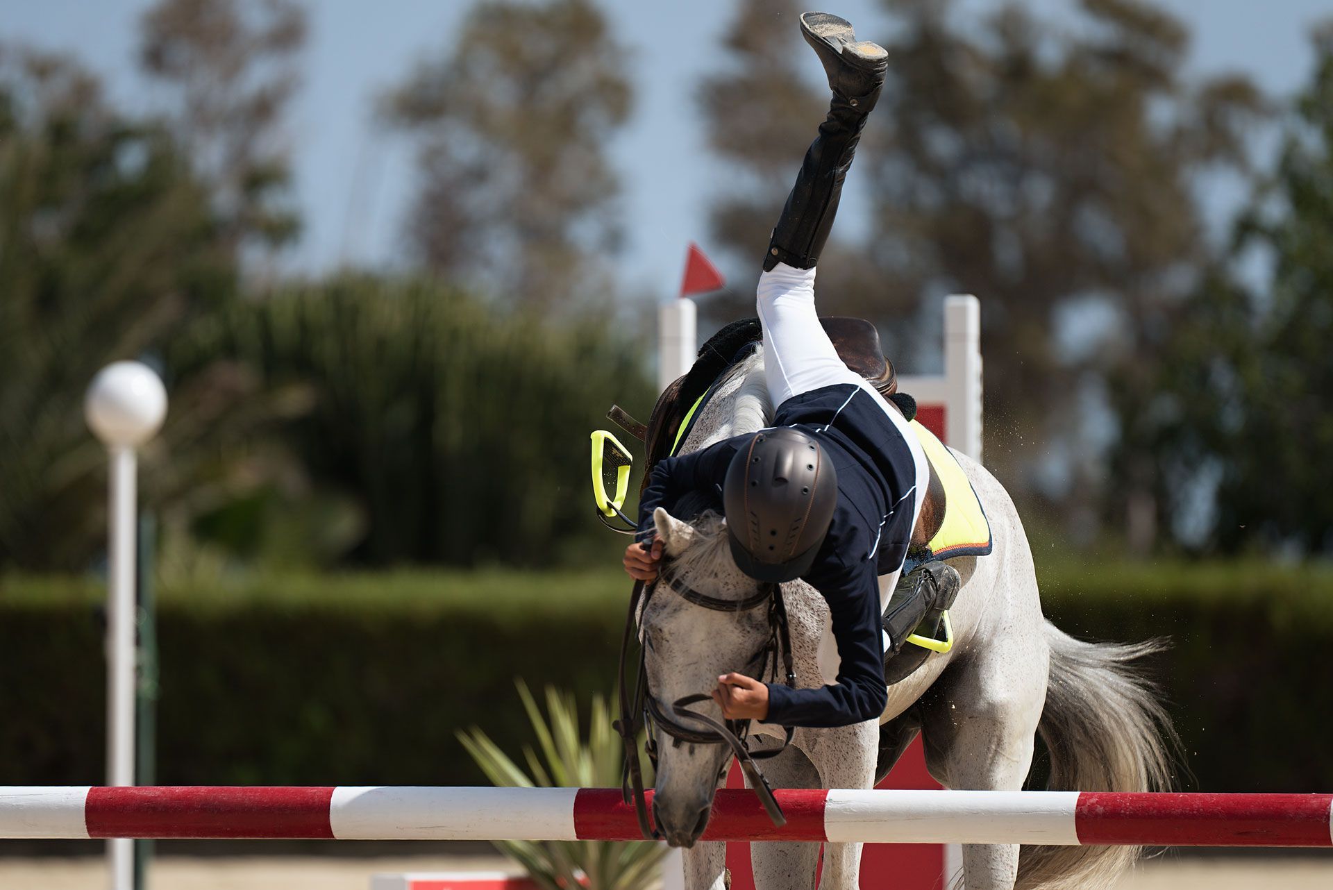 Equestrian rider falling over a jump; horse jumps clear. Blue and white uniform, outdoor competition.