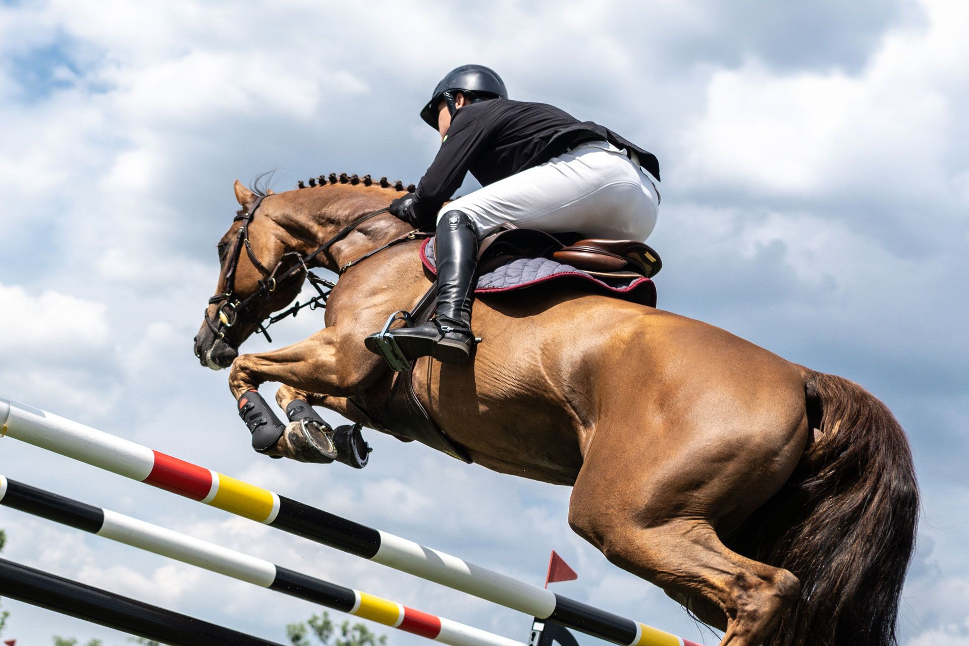 Horse and rider jumping over a multi-colored striped fence; blue sky background.