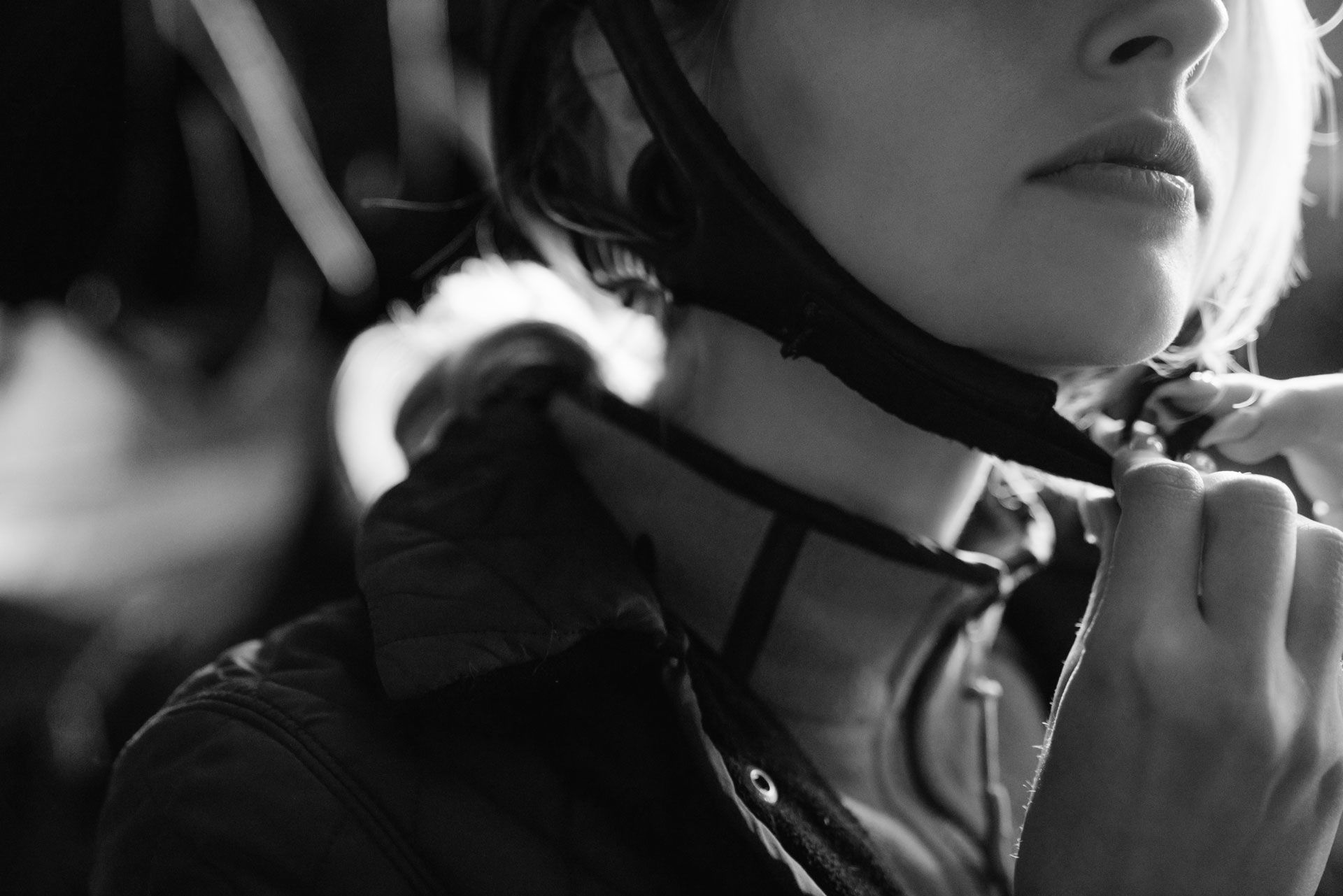 Woman fastening the strap of a riding helmet, close-up, black and white.