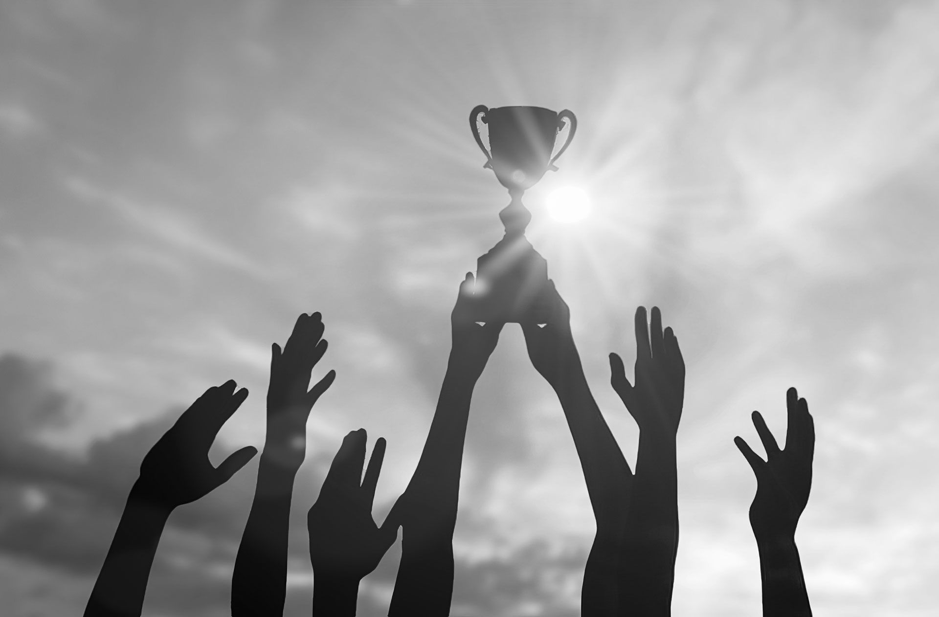 Silhouetted hands holding trophy toward bright sun in cloudy sky.