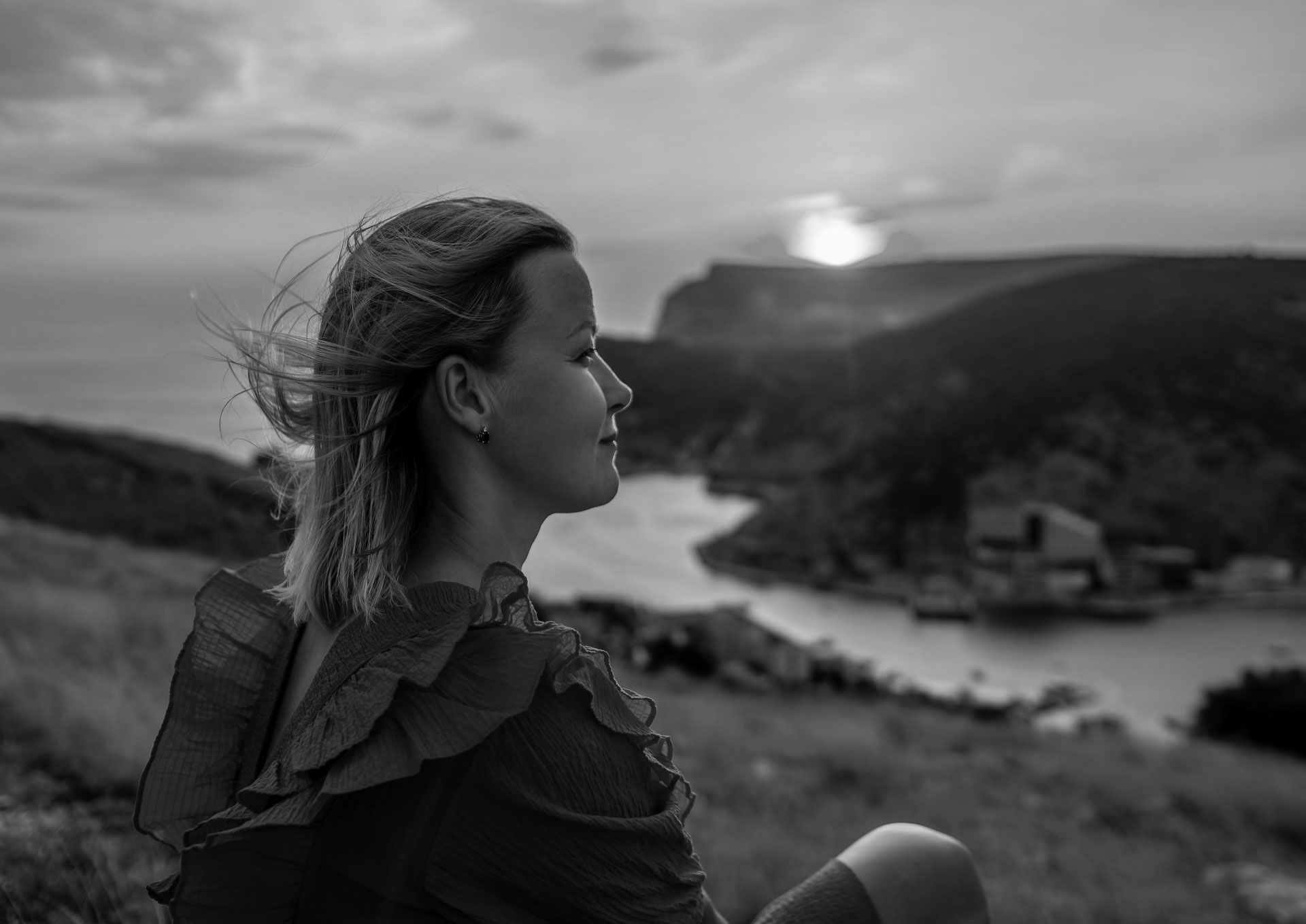 Woman gazing at sunset over a bay and hills. Black and white photo.