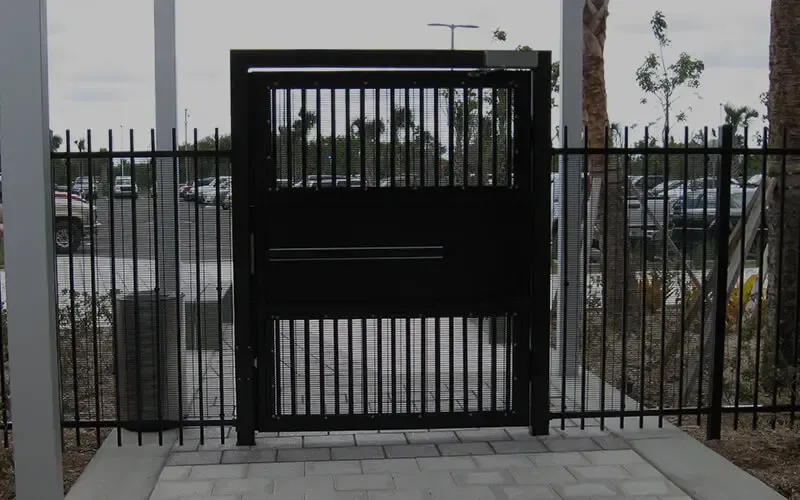 Black metal gate with vertical bars, set in a matching fence. Openings above and below a central horizontal bar.
