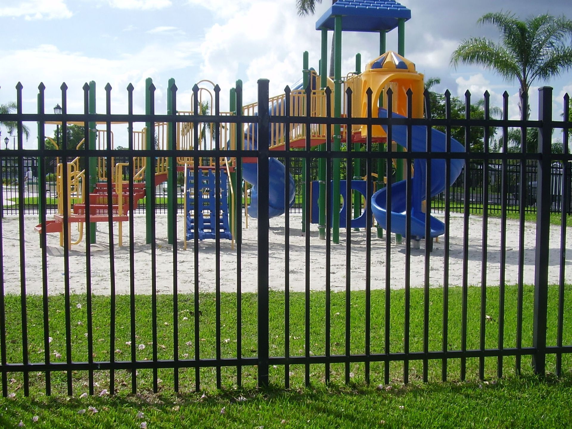 Black metal fence surrounding a playground with colorful slides and equipment.