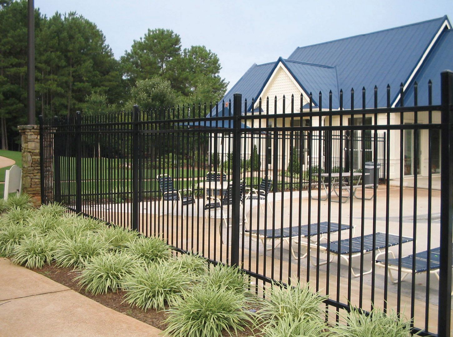 Black metal fence surrounds a patio with lounge chairs. Low plants line the base.