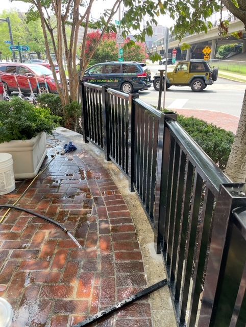 Black metal railing along a brick walkway; cars and street visible in background.
