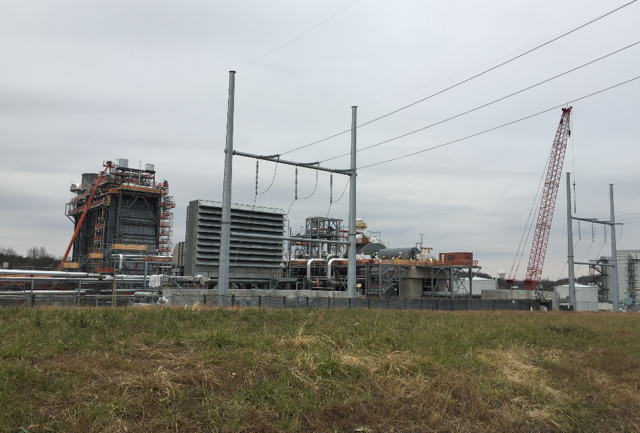Power plant construction site with crane and power lines against a cloudy sky.