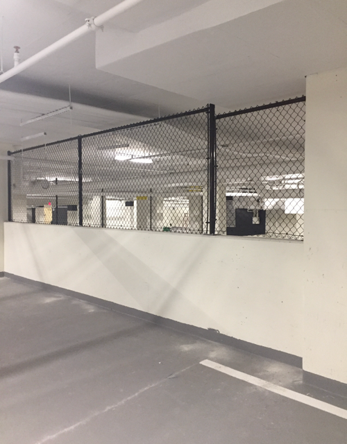 Parking garage with a chain-link fence on top of a concrete wall.