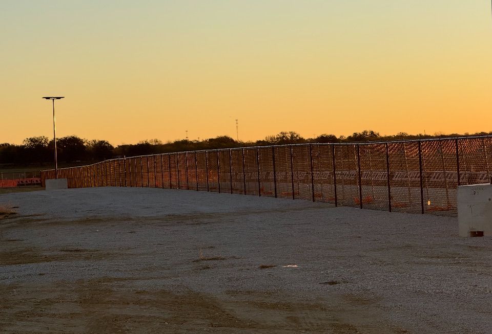 A chain-link fence on gravel with a sunset in the background.